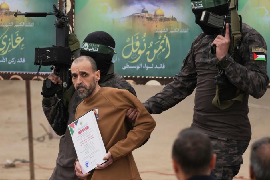 Two men with weapons and wearing masks escort a released hostage from a stage.