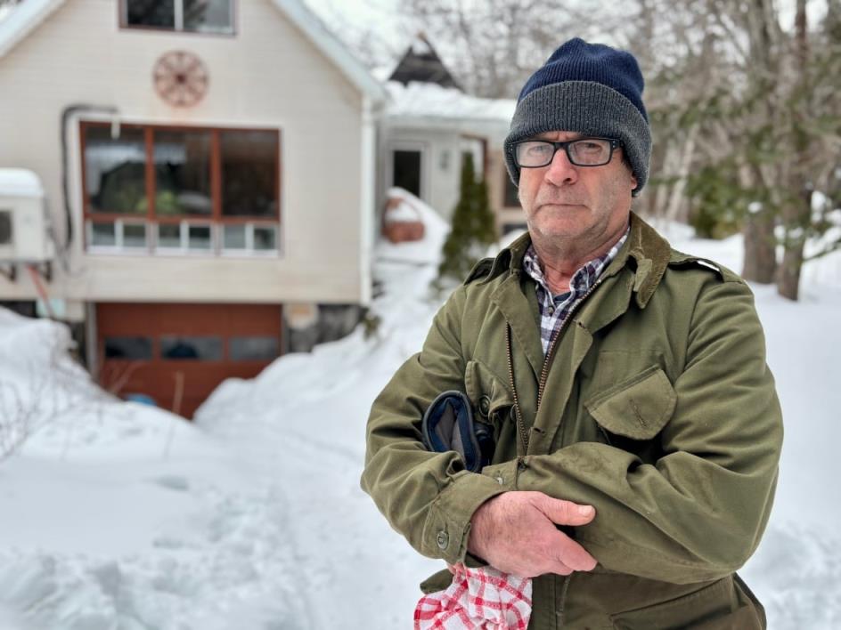 A man in winter clothing standing outside a house. He is looking at the camera.