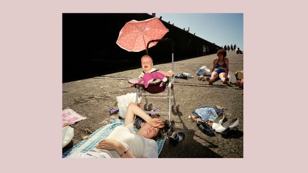 Photo of a tired-looking mother at a beach with her baby, who is crying